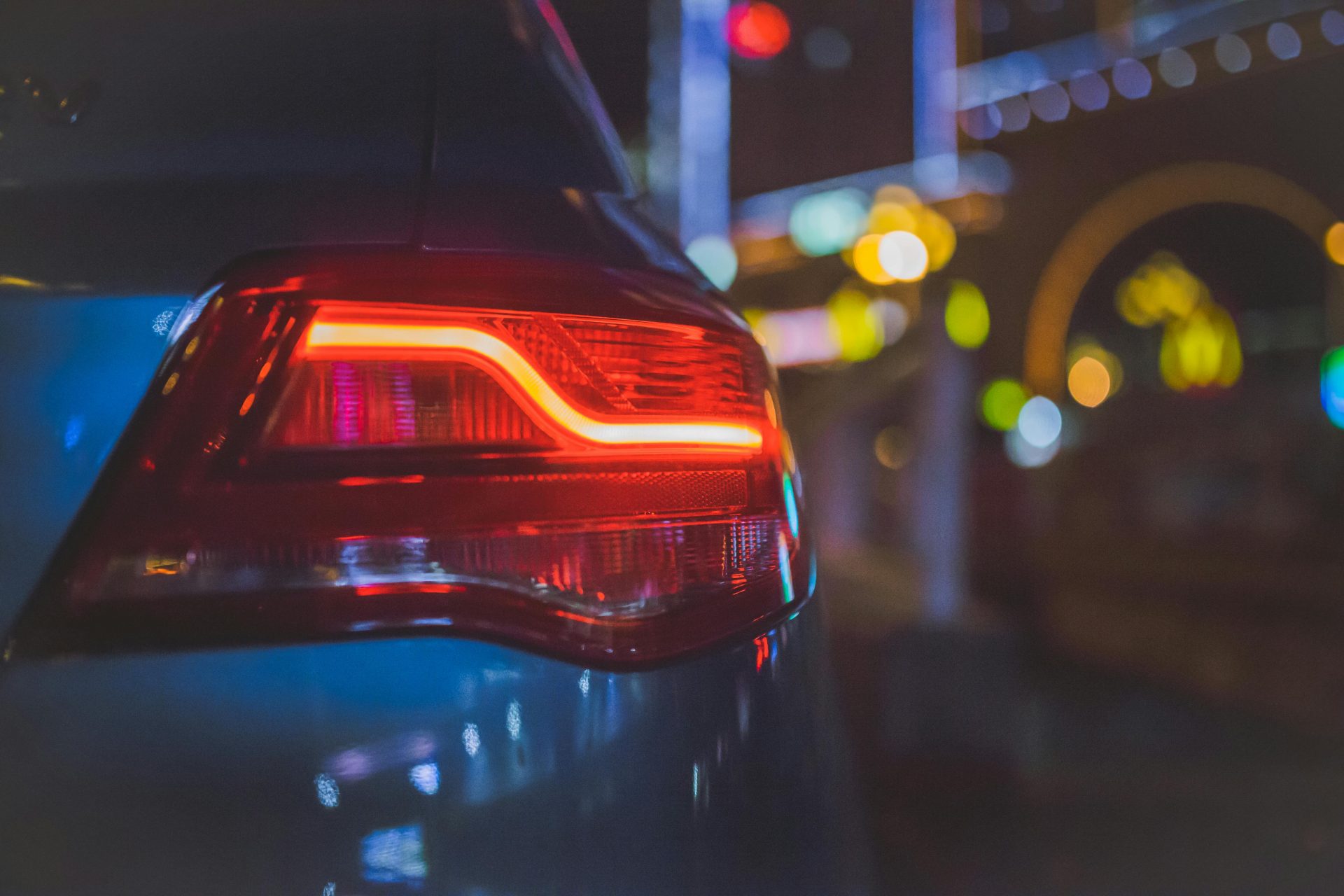 Close-up of a car's tail light with colorful bokeh background in an urban night setting.